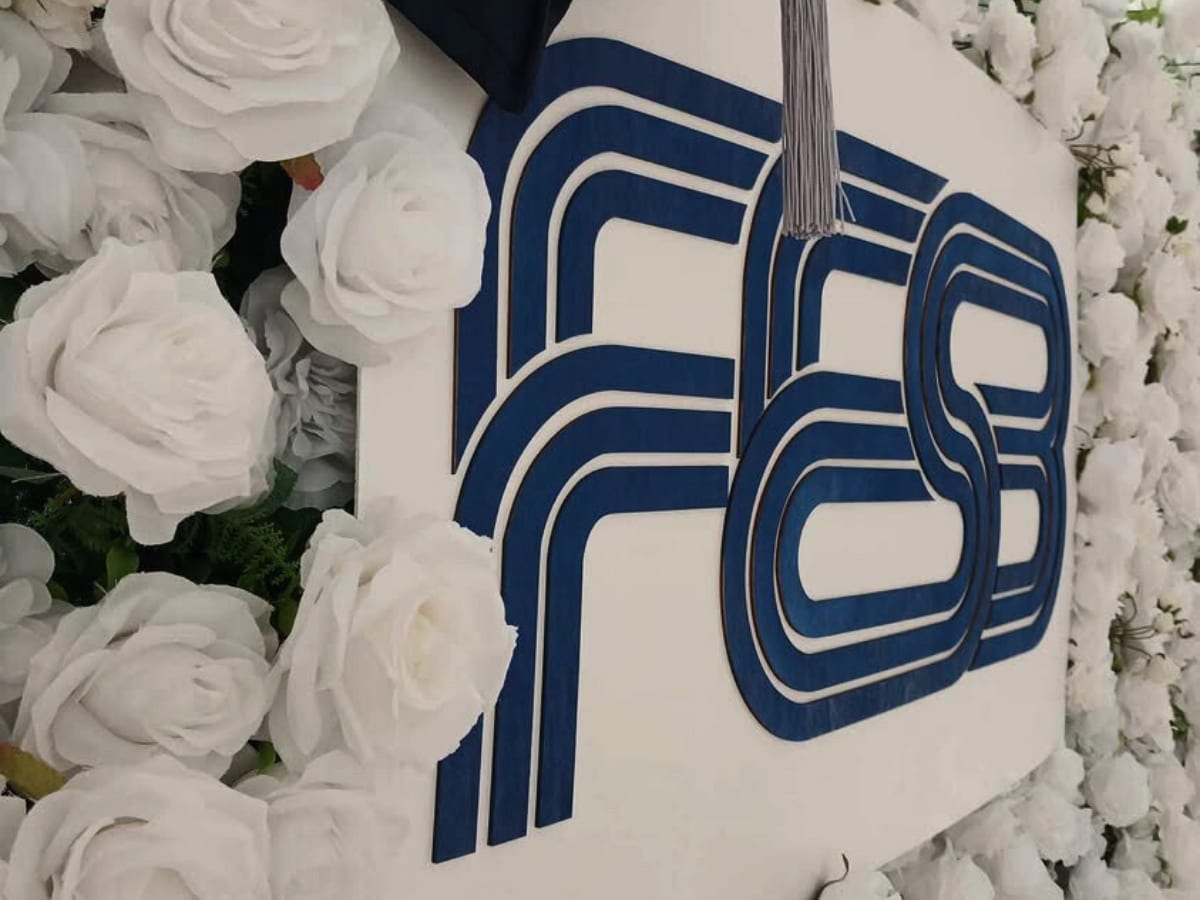 Krupni kadar 3D drvenog logotipa FESB u plavoj boji na bijeloj podlozi od umjetnog cvijeća.