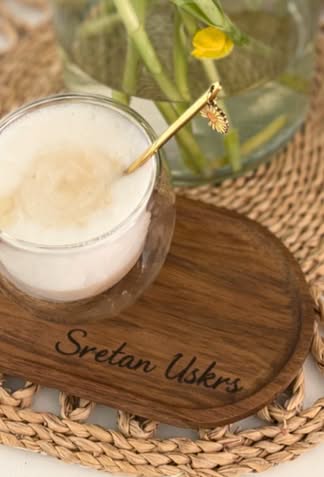 Ovalni drveni podmetač za kavu s ugraviranim natpisom Sretan Uskrs pored vaze s cvijećem na pletenom podlošku.